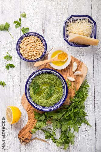 Homemade parsley pesto sauce and ingredients on white wooden background.