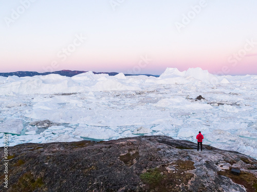 Travel in arctic landscape nature with icebergs - Greenland tourist explorer. Person looking at amazing Greenland icefjord - aerial photp. Man by ice and iceberg in Ilulissat. Climate change concept. photo