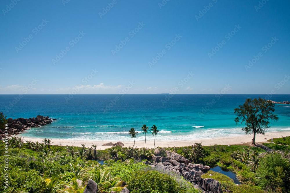 Idyllic tropical beach with rocks, palm trees, clear blue sky and horizon over the water in Grand Anse, La Digue island, Seychelles