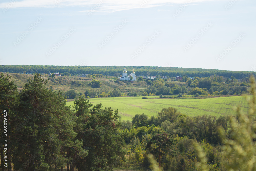 Rural landscape, lots of green grass and trees from which the Orthodox church looks out.