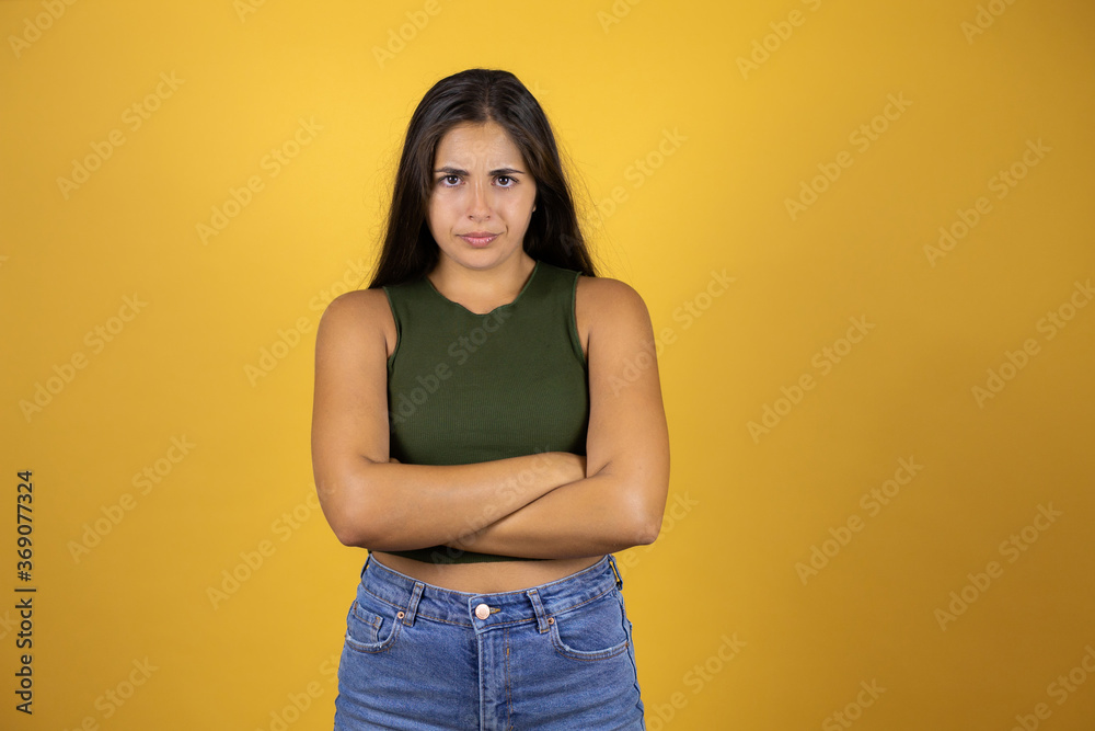 Young beautiful woman over yellow background skeptic and nervous, disapproving expression on face with crossed arms Young beautiful woman over yellow background skeptic and nervous, disapproving expression on face with crossed arms