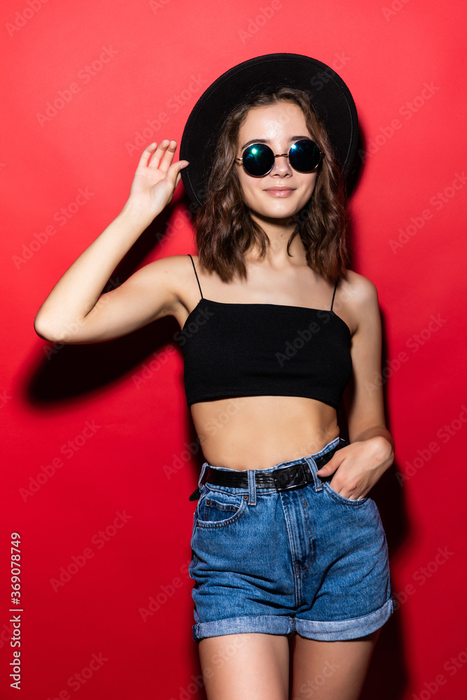 Young pretty girl wearing in sunglasses and floppy hat isolated on red background. Young pretty girl wearing in sunglasses and floppy hat isolated on red background.