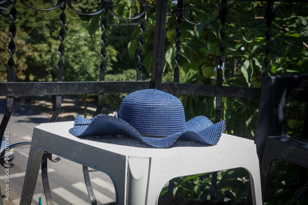 A blue hat (women's) on the white table on the balcony with the view on the street
