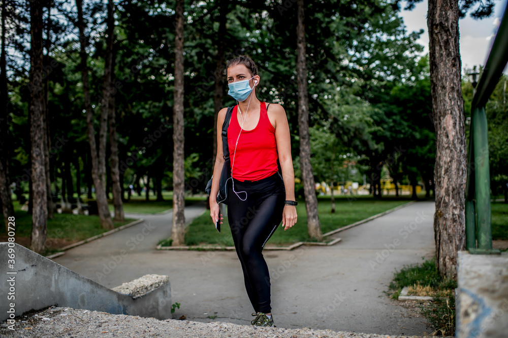 Young Caucasian woman with protective face mask on her way to training in a public park. Young Caucasian woman with protective face mask on her way to training in a public park.