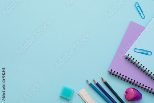 Education flat lay. Top view of blue and purple notebooks, pencil sharpener, clips, eraser, ruler and color pencils. Copy space. 