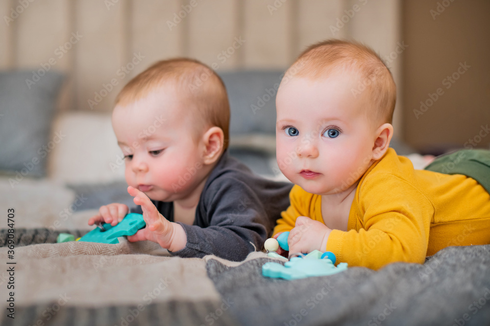 Twin girls lie on the bed for five months and gnaw on teething. Babies are teething. The girls look into the frame. Twin girls lie on the bed for five months and gnaw on teething. Babies are teething. The girls look into the frame.
