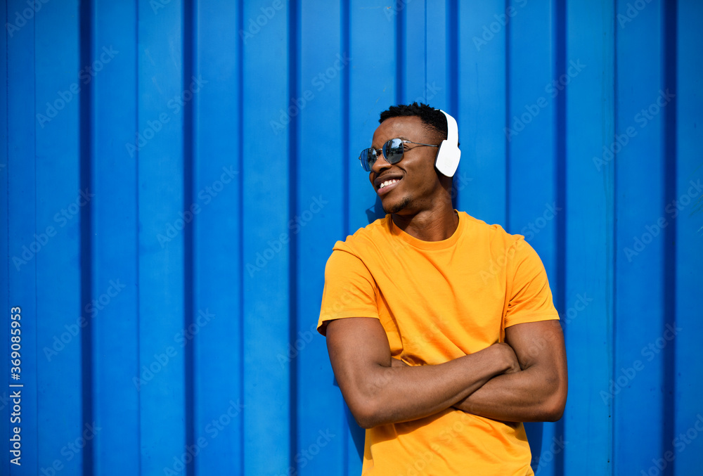 Fototapeta premium Young black man with headphones standing against blue background, black lives matter concept.