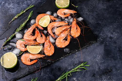 Fresh large shrimp with lime, sprigs of razmarin, ice on a dark background, close-up. Seafood