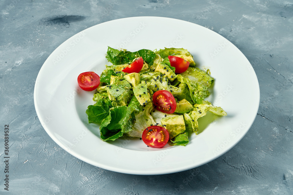 Vegetarian salad with avocado, lettuce and cherry tomatoes in a white plate on a concrete background Vegetarian salad with avocado, lettuce and cherry tomatoes in a white plate on a concrete background