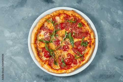Italian pizza with salami, arugula and parmesan on a white plate. Concrete background. Top view