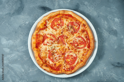 Classic italian pizza margarita with tomatoes and cheese in a white plate on a concrete background