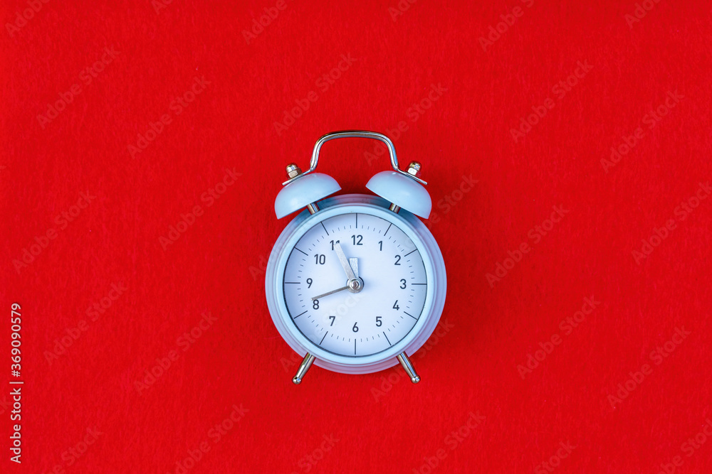 Blue retro alarm clock on red background with copy space. Concept of time, 5 minutes to 12, until the New year Blue retro alarm clock on red background with copy space. Concept of time, 5 minutes to 12, until the New year