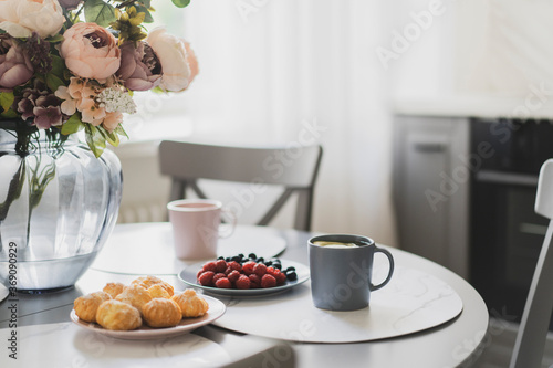 Wallpaper Mural Beautiful breakfast on table near window in white kitchen - cups of tea, flowers, berries, snacks. Healthy, romantic meal in modern room interior. Stylish room interior with natural morning light. Torontodigital.ca