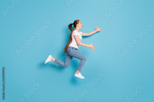 Full length profile side photo of excited energetic girl jump run want hug long wait friend wear white t-shirt sneakers isolated over blue color background