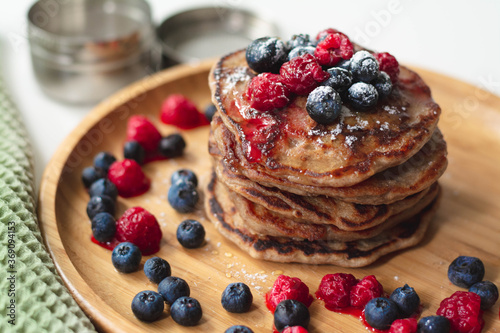 A heap of healthy vegan gluten-free whole grain pancakes made with buckwheat flour topped with raspberries and blueberries with icing sugar sprinkled on top 
