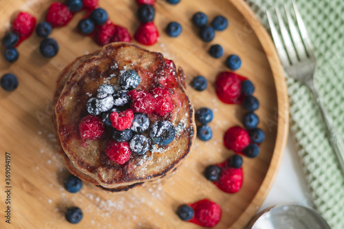 A heap of healthy vegan gluten-free whole grain pancakes made with buckwheat flour topped with raspberries and blueberries with icing sugar sprinkled on top 