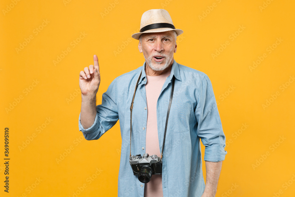 Excited traveler tourist elderly gray-haired man in hat isolated on yellow wall background. Passenger traveling abroad on weekends getaway. Air flight journey concept. Holding finger up with new idea.