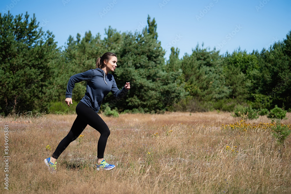 Young woman running on a natural meadow in the background of green trees and blue sky Young woman running on a natural meadow in the background of green trees and blue sky