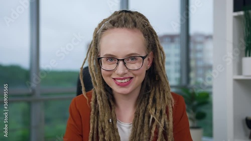 Attractive confident professional young woman with dreadlocks in glasses posing on camera with sincerely smile in modern office photo