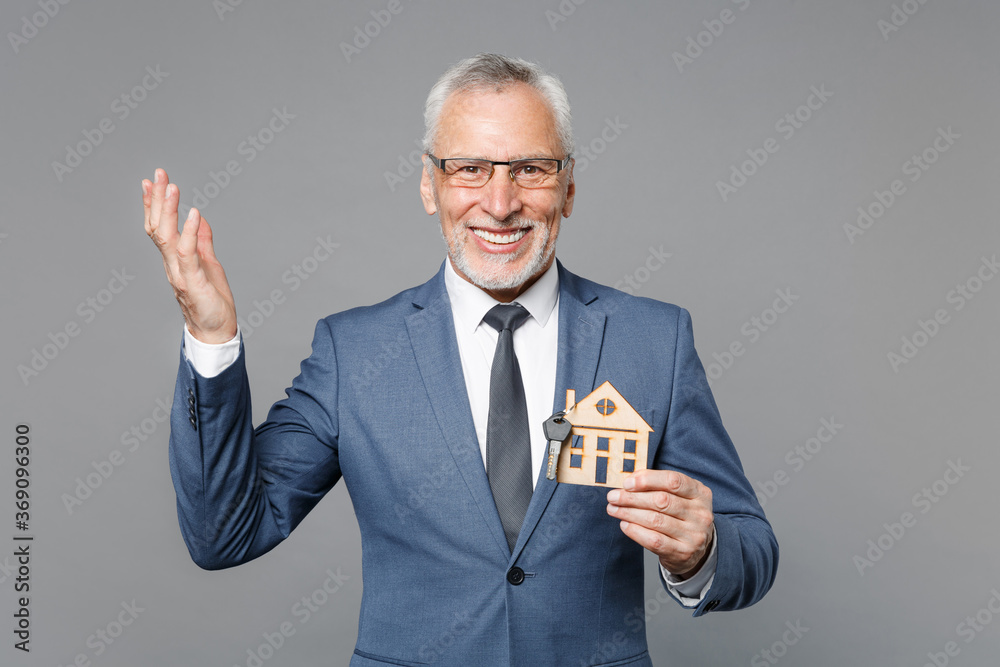 Excited elderly gray-haired mustache bearded business man in blue suit shirt tie isolated on grey background. Achievement career wealth business concept. Hold house, bunch of keys, spreading hands. Excited elderly gray-haired mustache bearded business man in blue suit shirt tie isolated on grey background. Achievement career wealth business concept. Hold house, bunch of keys, spreading hands.