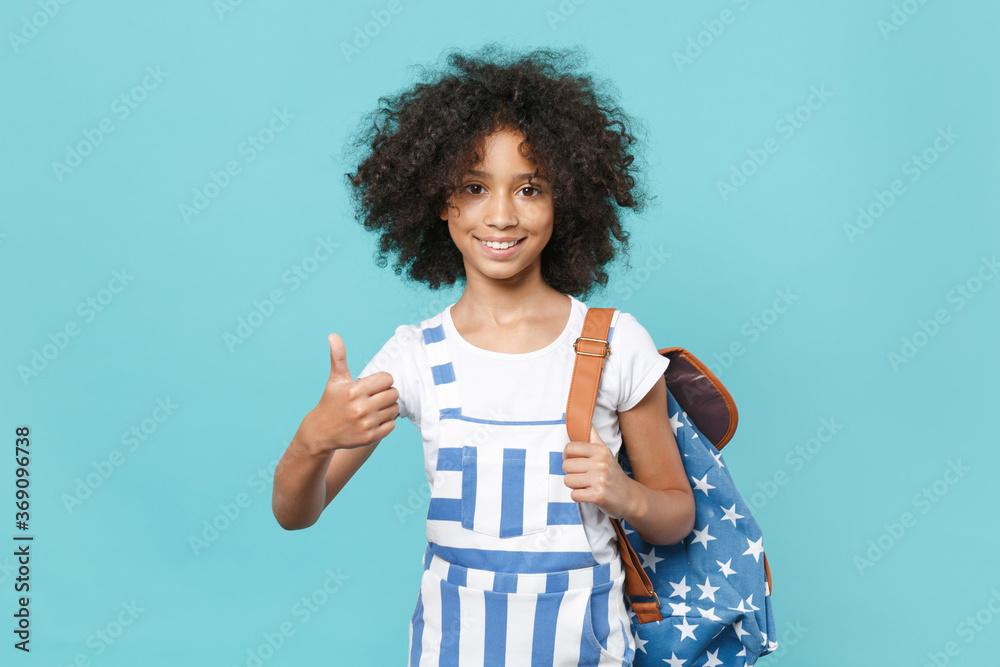 Smiling little african american kid schoolgirl 12-13 years old in striped clothes with backpack isolated on blue background. Childhood education in school concept. Mock up copy space Showing thumb up. Smiling little african american kid schoolgirl 12-13 years old in striped clothes with backpack isolated on blue background. Childhood education in school concept. Mock up copy space Showing thumb up.