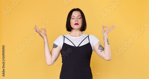 A young and not ordinary hipster woman with tattoos meditates and relaxes on a yellow background. Calm and balance concept. photo