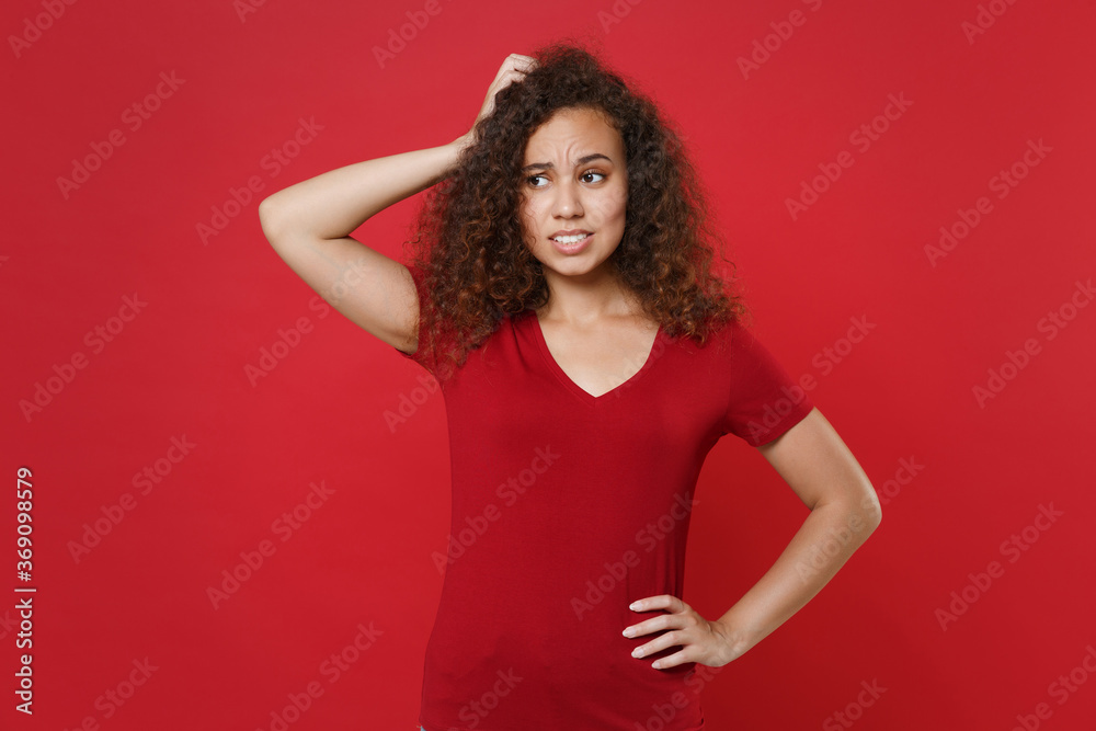 Preoccupied young african american woman girl in casual t-shirt posing isolated on red wall background studio portrait. People lifestyle concept. Mock up copy space. Put hand on head, looking aside. Preoccupied young african american woman girl in casual t-shirt posing isolated on red wall background studio portrait. People lifestyle concept. Mock up copy space. Put hand on head, looking aside.