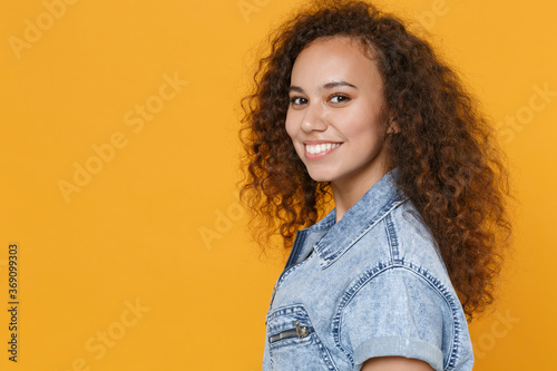 Side view of smiling young african american woman girl in casual denim clothes isolated on yellow background studio portrait. People emotions lifestyle concept. Mock up copy space. Looking camera. © ViDi Studio