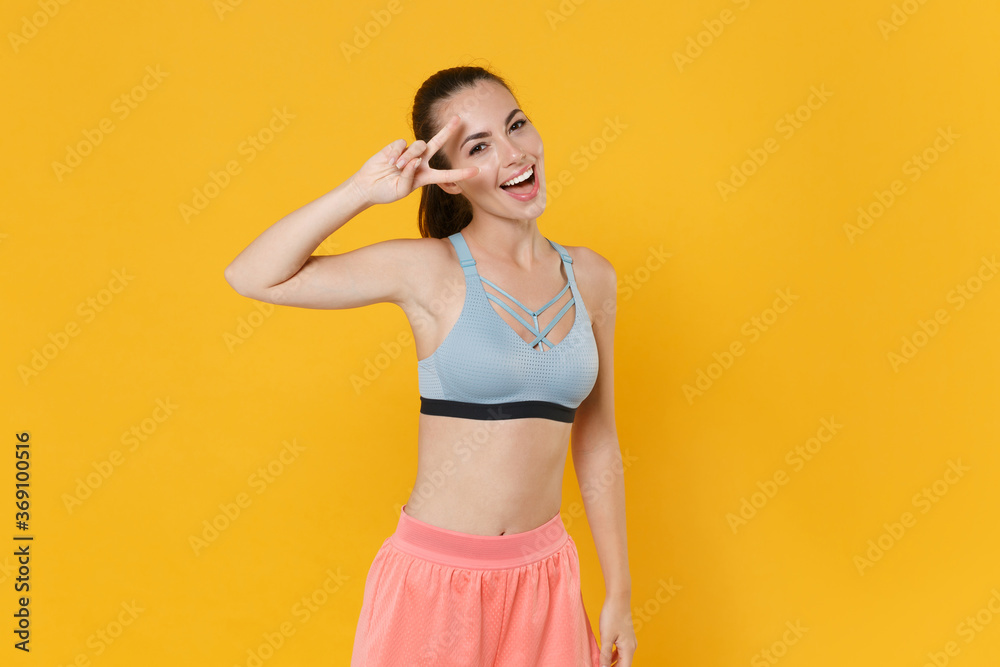Cheerful young fitness sporty woman girl in sportswear working out isolated on yellow background studio portrait. Workout sport motivation lifestyle concept. Mock up copy space. Showing victory sign.