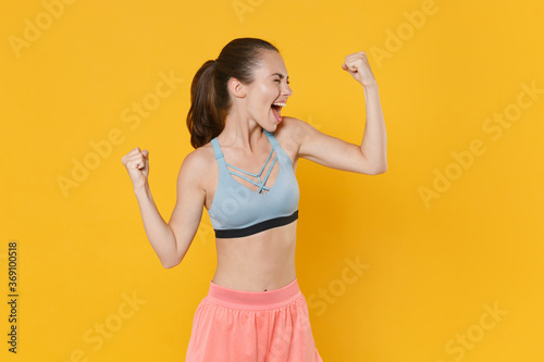 Joyful young fitness sporty woman girl in sportswear working out isolated on yellow wall background studio. Workout sport motivation lifestyle concept. Clenching fists like winner keeping eyes closed.