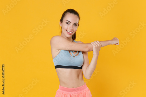 Smiling young fitness sporty woman girl in sportswear posing working out isolated on yellow wall background studio. Workout sport motivation concept. Mock up copy space. Doing stretching exercising. © ViDi Studio