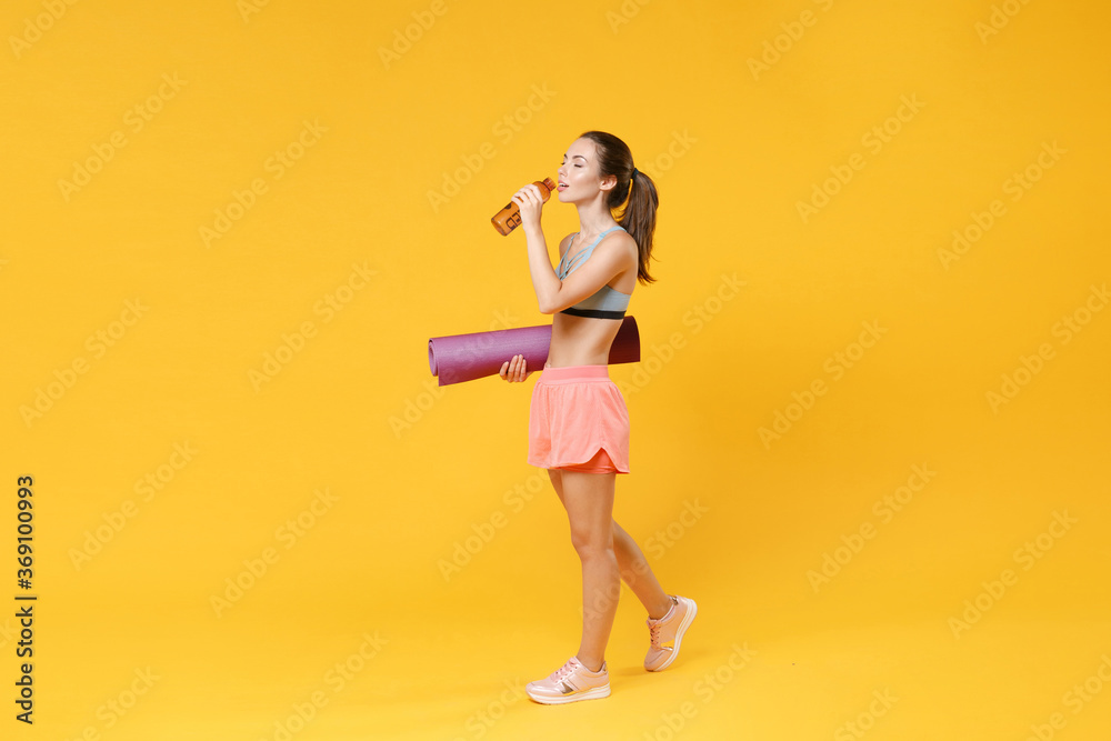 Full length portrait of beautiful young fitness woman girl in sportswear working out isolated on yellow background studio. Workout sport motivation lifestyle concept. Hold yoga mat, bottle of water. Full length portrait of beautiful young fitness woman girl in sportswear working out isolated on yellow background studio. Workout sport motivation lifestyle concept. Hold yoga mat, bottle of water.