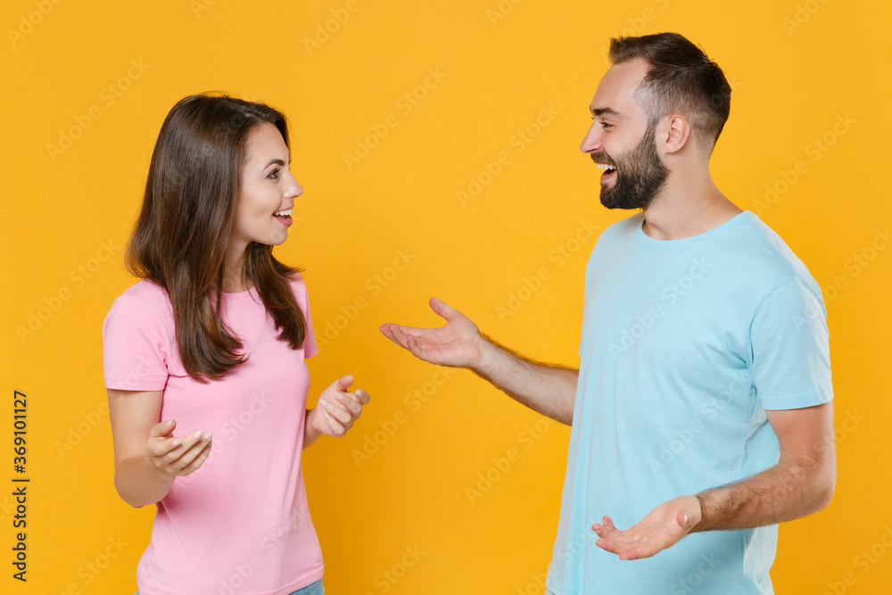 Cheerful young couple two friends guy girl in blue pink t-shirts isolated on yellow background studio portrait. People lifestyle concept. Mock up copy space. Speaking talking, looking at each other. Cheerful young couple two friends guy girl in blue pink t-shirts isolated on yellow background studio portrait. People lifestyle concept. Mock up copy space. Speaking talking, looking at each other.