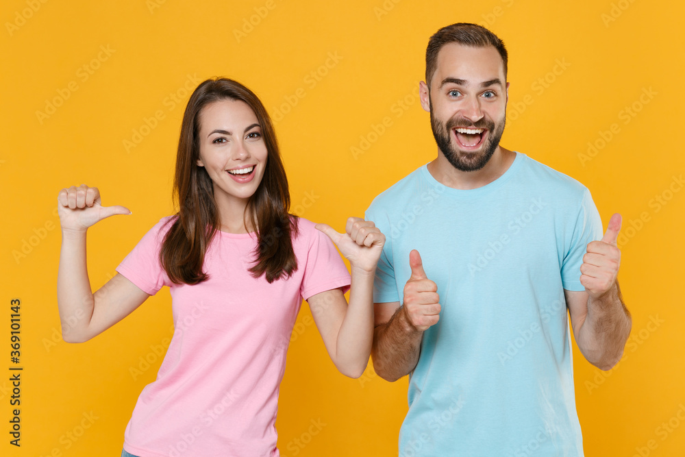 Cheerful young couple friends guy girl in blue pink t-shirts isolated on yellow background studio portrait. People lifestyle concept. Mock up copy space. Pointing thumbs on herself, showing thumbs up. Cheerful young couple friends guy girl in blue pink t-shirts isolated on yellow background studio portrait. People lifestyle concept. Mock up copy space. Pointing thumbs on herself, showing thumbs up.