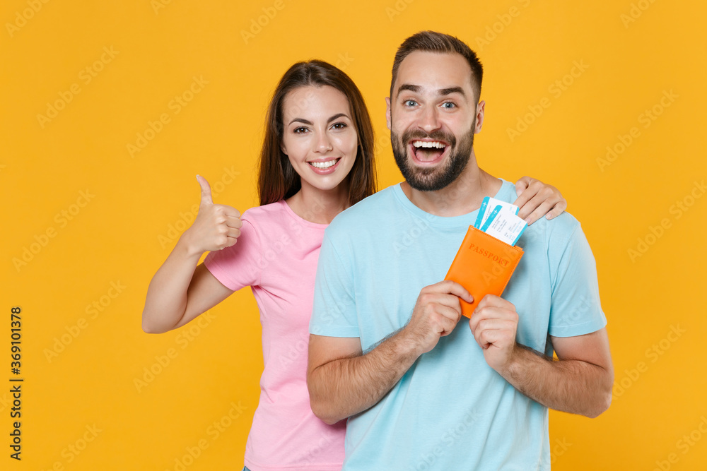 Excited young couple friends guy girl in t-shirts isolated on yellow background. Passenger traveling abroad on weekends getaway. Air flight journey concept. Hold passport tickets, showing thumb up. Excited young couple friends guy girl in t-shirts isolated on yellow background. Passenger traveling abroad on weekends getaway. Air flight journey concept. Hold passport tickets, showing thumb up.
