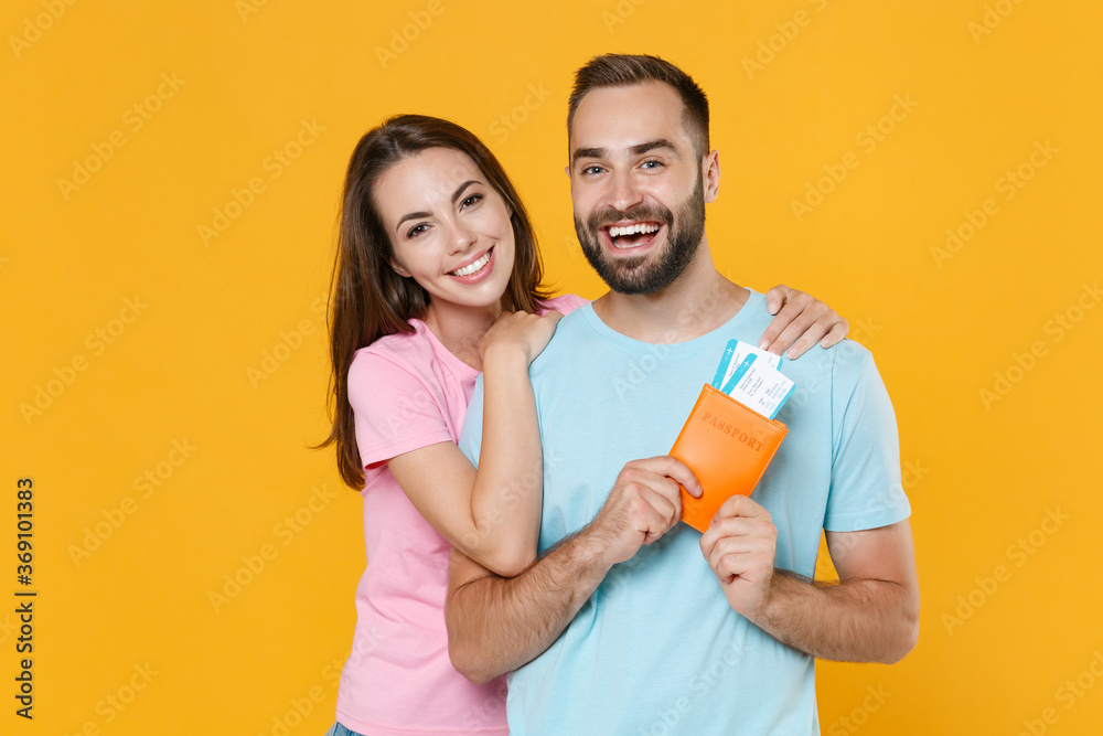 Cheerful young couple friends guy girl in blue pink t-shirts isolated on yellow background. Passenger traveling abroad on weekends getaway. Air flight journey concept. Hold passport tickets, hugging. Cheerful young couple friends guy girl in blue pink t-shirts isolated on yellow background. Passenger traveling abroad on weekends getaway. Air flight journey concept. Hold passport tickets, hugging.
