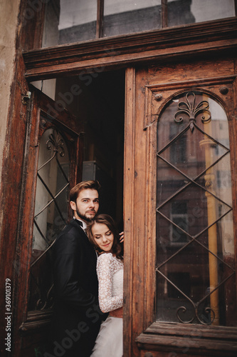 Beautiful newlyweds hugging near the ancient door. Wedding portrait of a stylish groom and a young bride near old house in in a European town © Andriy Medvediuk