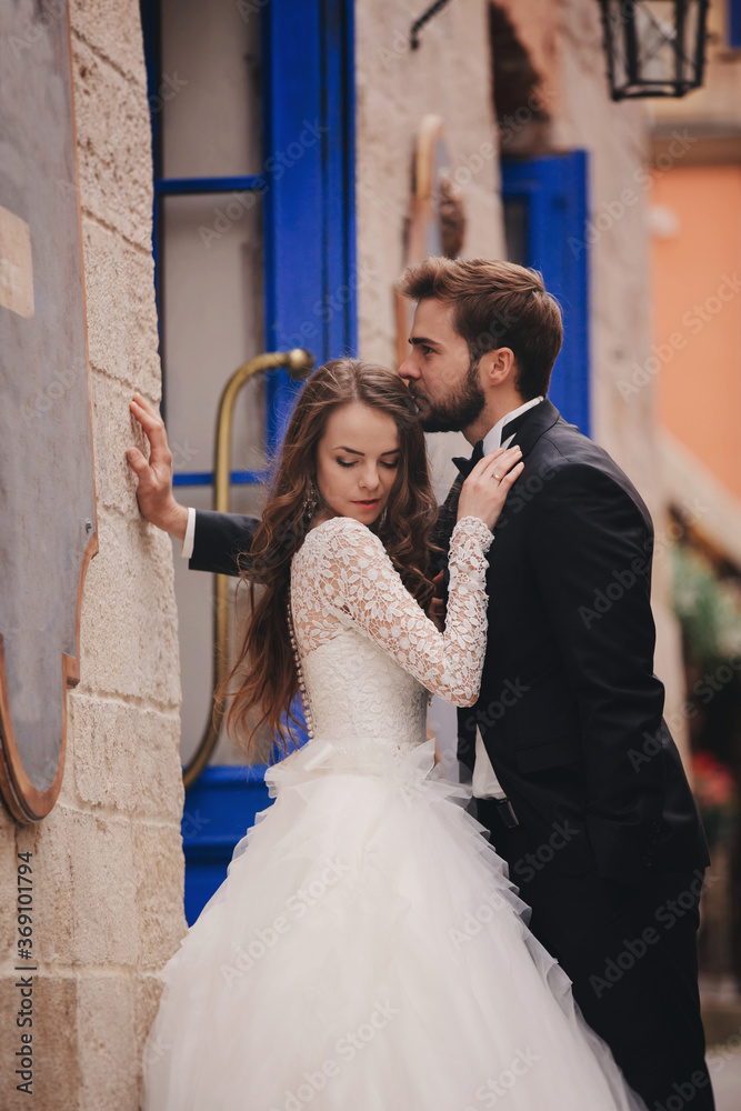 Wedding couple hugging in the old city. Blue vintage doors and cafe in ancient town on background. stylish bride in white long dress and groom in suit and bow tie. wedding day Wedding couple hugging in the old city. Blue vintage doors and cafe in ancient town on background. stylish bride in white long dress and groom in suit and bow tie. wedding day
