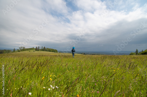 mother with baby walks on a green meadow overlooking the valley and the cloudy sky