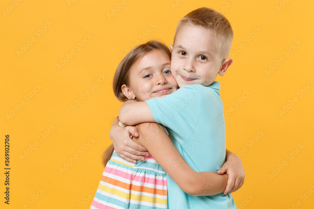 Little couple kids boy girl 5-6 years old in blue pink clothes shirt dress posing have fun isolated on yellow background children studio portrait. People childhood lifestyle concept embrace hug love Little couple kids boy girl 5-6 years old in blue pink clothes shirt dress posing have fun isolated on yellow background children studio portrait. People childhood lifestyle concept embrace hug love