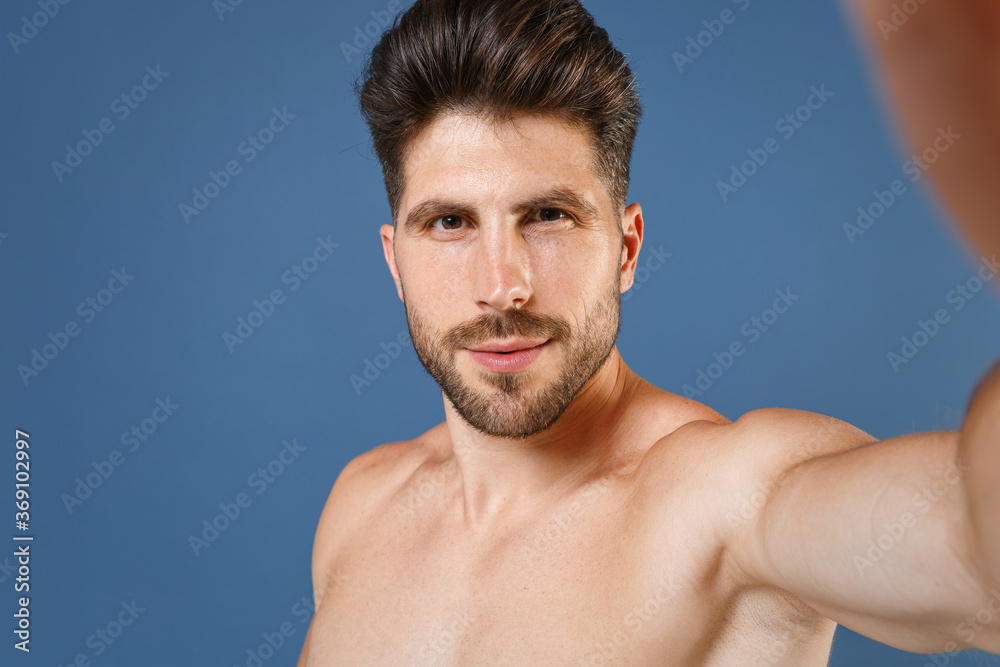 Close up of handsome bearded fitness sporty strong guy bare-chested muscular sportsman isolated on blue wall background. Workout sport motivation lifestyle concept. Doing selfie shot on mobile phone. Close up of handsome bearded fitness sporty strong guy bare-chested muscular sportsman isolated on blue wall background. Workout sport motivation lifestyle concept. Doing selfie shot on mobile phone.