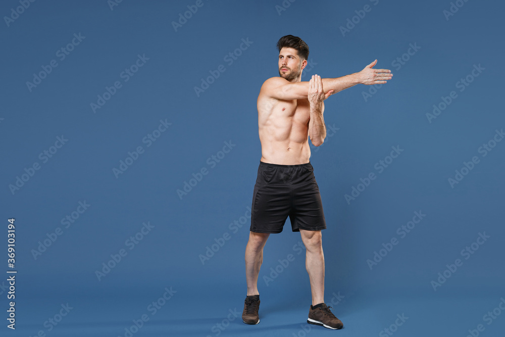 Full length portrait of young bearded fitness sporty strong guy bare-chested muscular sportsman isolated on blue background. Workout sport motivation lifestyle concept. Doing stretching exercising. Full length portrait of young bearded fitness sporty strong guy bare-chested muscular sportsman isolated on blue background. Workout sport motivation lifestyle concept. Doing stretching exercising.