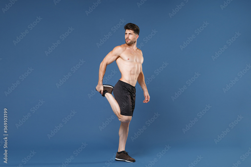 Full length portrait of young fitness sporty strong guy bare-chested muscular sportsman isolated on blue background. Workout sport motivation lifestyle concept. Doing stretching exercising for legs. Full length portrait of young fitness sporty strong guy bare-chested muscular sportsman isolated on blue background. Workout sport motivation lifestyle concept. Doing stretching exercising for legs.
