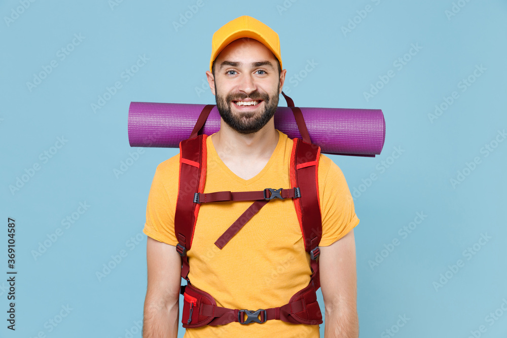Smiling traveler young man in yellow casual t-shirt, cap with backpack isolated on blue background studio. Tourist traveling on weekends getaway. Tourism discovering hiking concept. Looking camera. Smiling traveler young man in yellow casual t-shirt, cap with backpack isolated on blue background studio. Tourist traveling on weekends getaway. Tourism discovering hiking concept. Looking camera.
