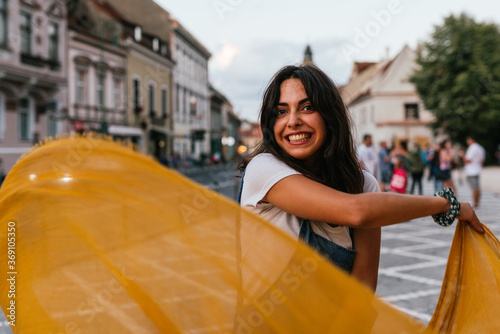 Smiling young woman moving a yellow fabric to wind. photo