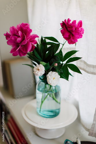 Tiny roses and pink peonies in blue glass jar on windowsill seen from above