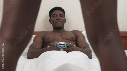Close up of unrecognizable spreading black legs of girl. On the background lying African man and playing console. Woman takes off her panties. Dumbfounded guy throws joystick