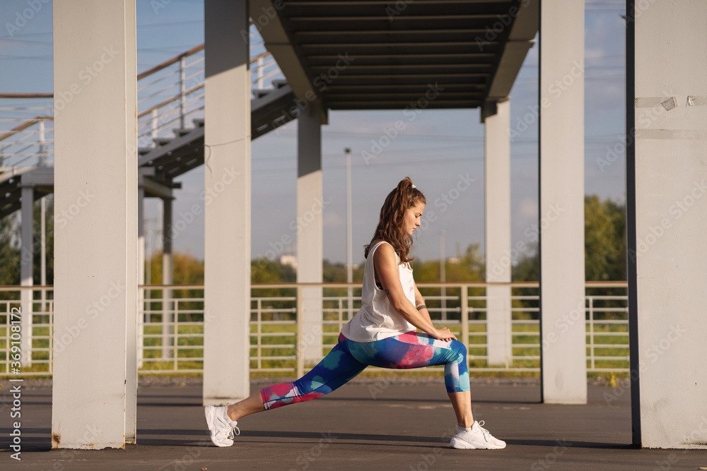 Concentrated female athlete stretching legs on sports ground Concentrated female athlete stretching legs on sports ground