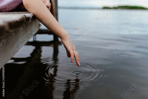 A girl dips her hand into lake water leaving ripples in concentric circles