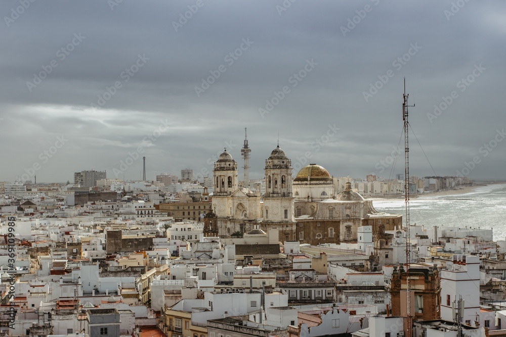 Aerial dramatic panoramic view of the old city, rooftops and Cathedral de Santa Cruz in cloudy day from tower Tavira in Cadiz, Andalusia, Spain.European cityscape.Beautiful white city by sea